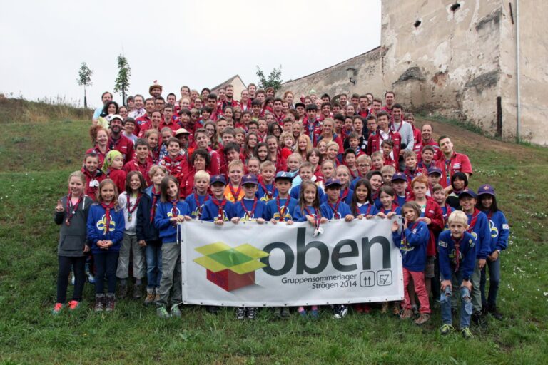 Großes Gruppenfoto von Pfadfinder*innen in roten und blauen Uniformen beim Sommerlager „oben“ 2014 in Strögen
